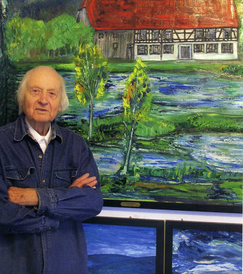 Das Bild zeigt den Künstler Rudolf Schieder vor einem seiner Gemälde